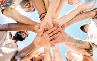 Low angle shot of a group of friends standing together and stacking their hands in the middle