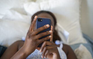 Close-up of a young teenage girl using a smart phone while lying on her bed